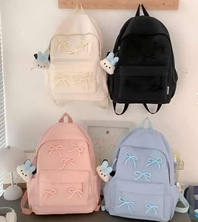 Cuatro mochilas: crema, negra, rosa y azul, cada una con detalles de lazos y adornos de conejito.