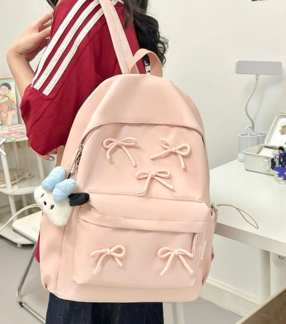 Mochila de color rosa decorada con lazos, sostenida por una persona que viste una camiseta de rayas rojas y blancas.