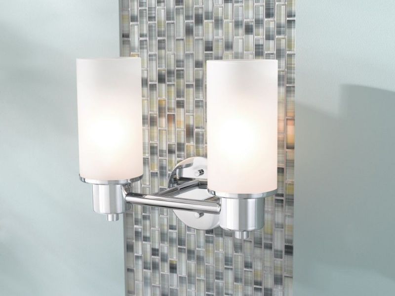 A bathroom wall light with two white glass shades on a tiled wall.