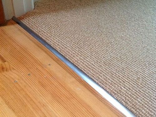 There is a wooden floor next to a carpeted floor.