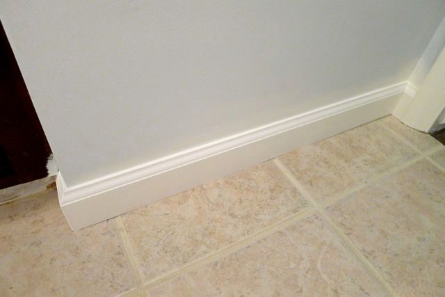 A white molding on a tiled floor next to a white wall.