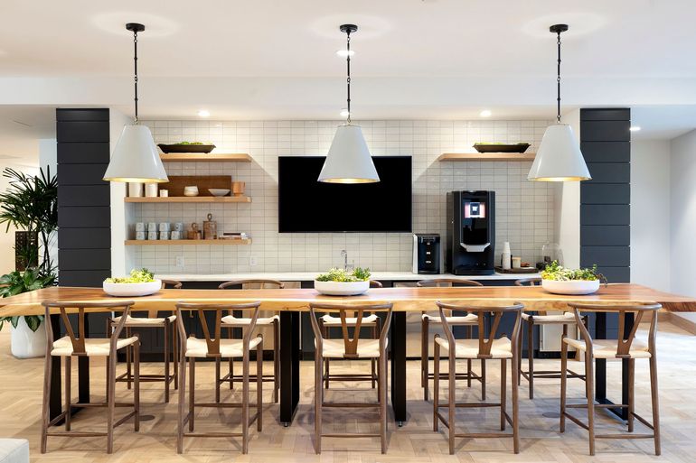 Communal kitchen area with a large wooden table, bar stools, and pendant lights.