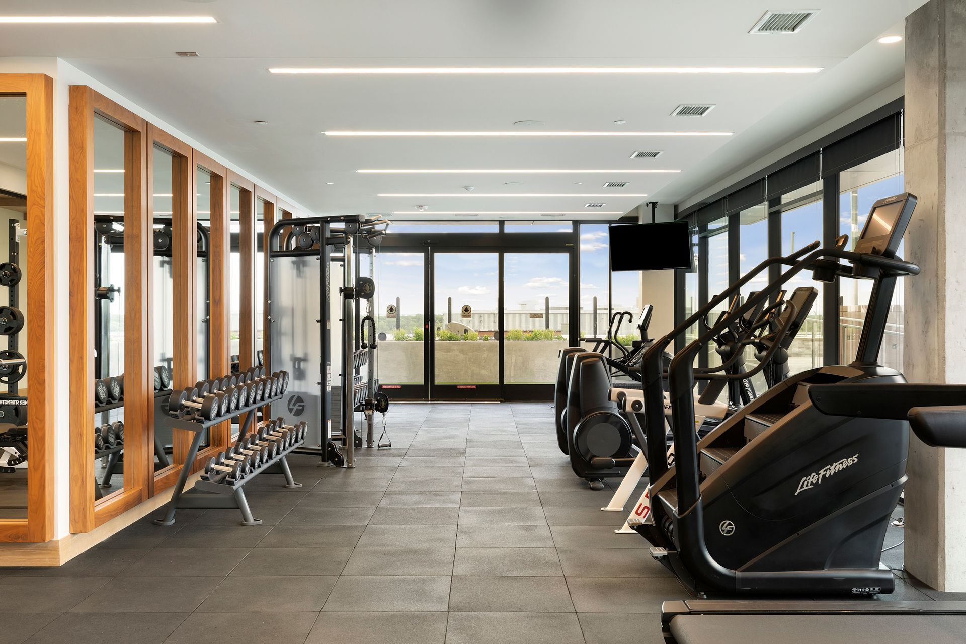 Gym with weights, machines, and large windows overlooking an outdoor view.