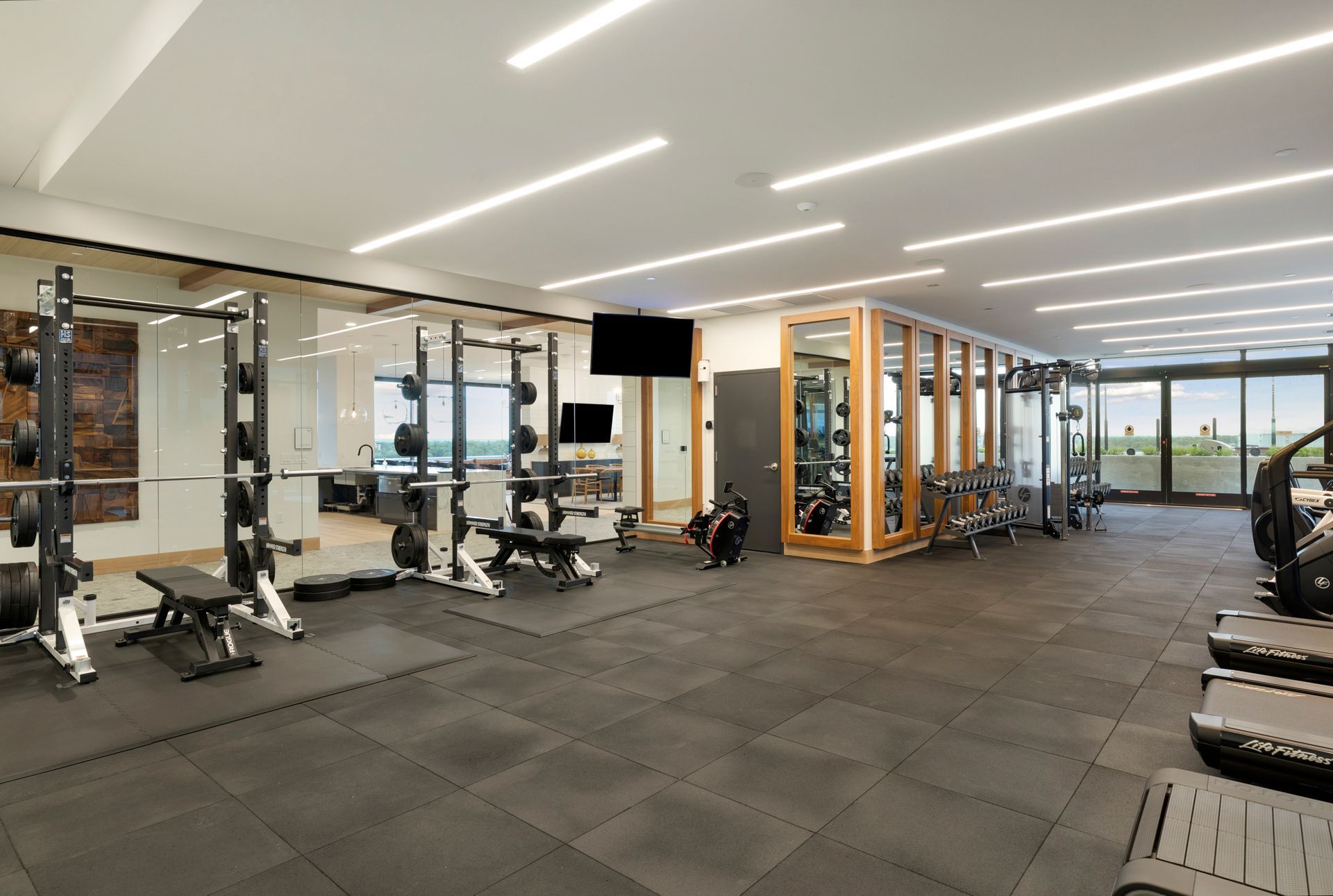 Gym interior with weight racks, benches, and equipment; neutral tones, focused on fitness.