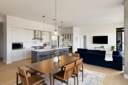 Open-concept kitchen and living room. Dining table, blue couch, white cabinets, gray island, and wood flooring.