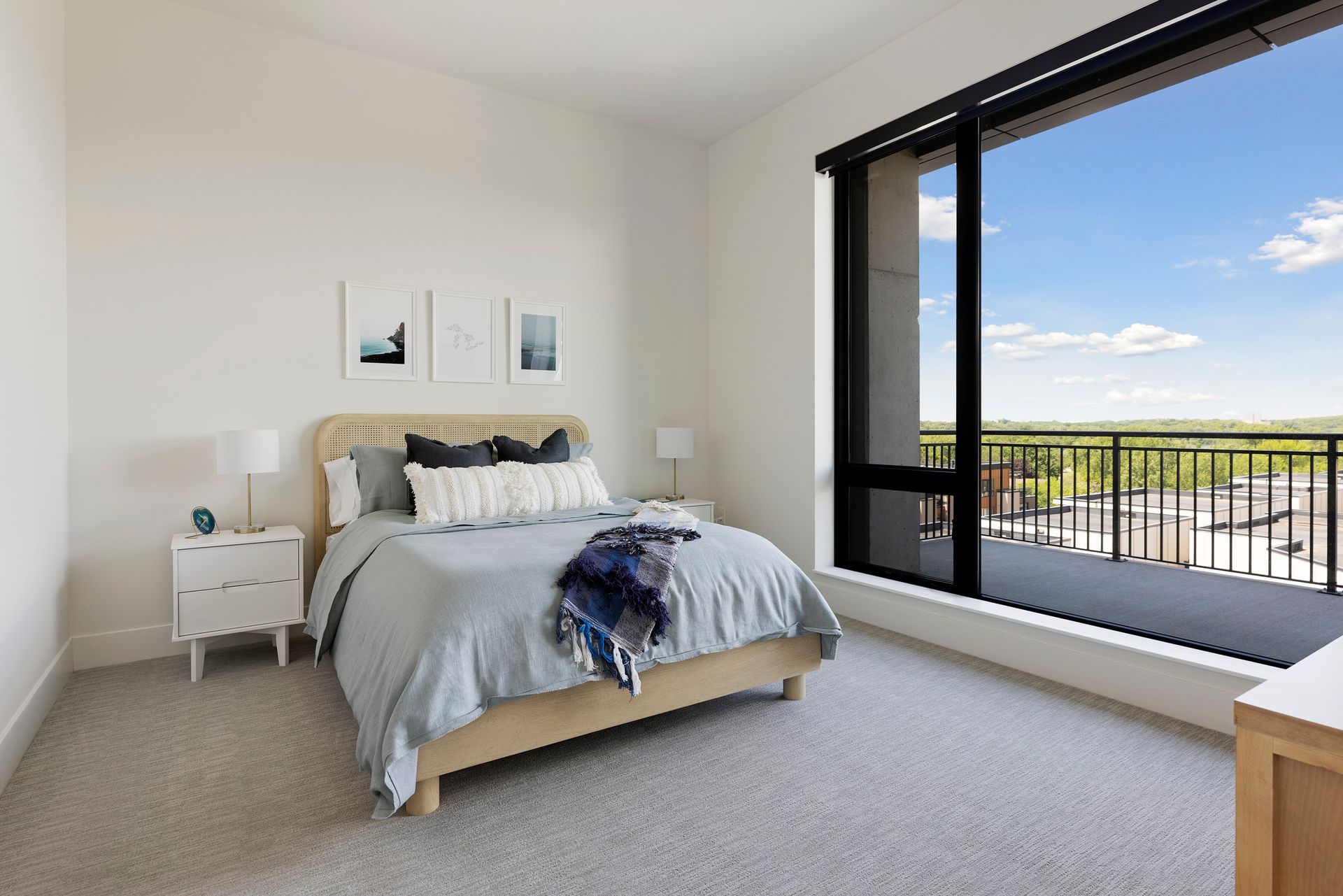 Bedroom with bed, nightstands, large window overlooking a cityscape, neutral colors, and wall art.