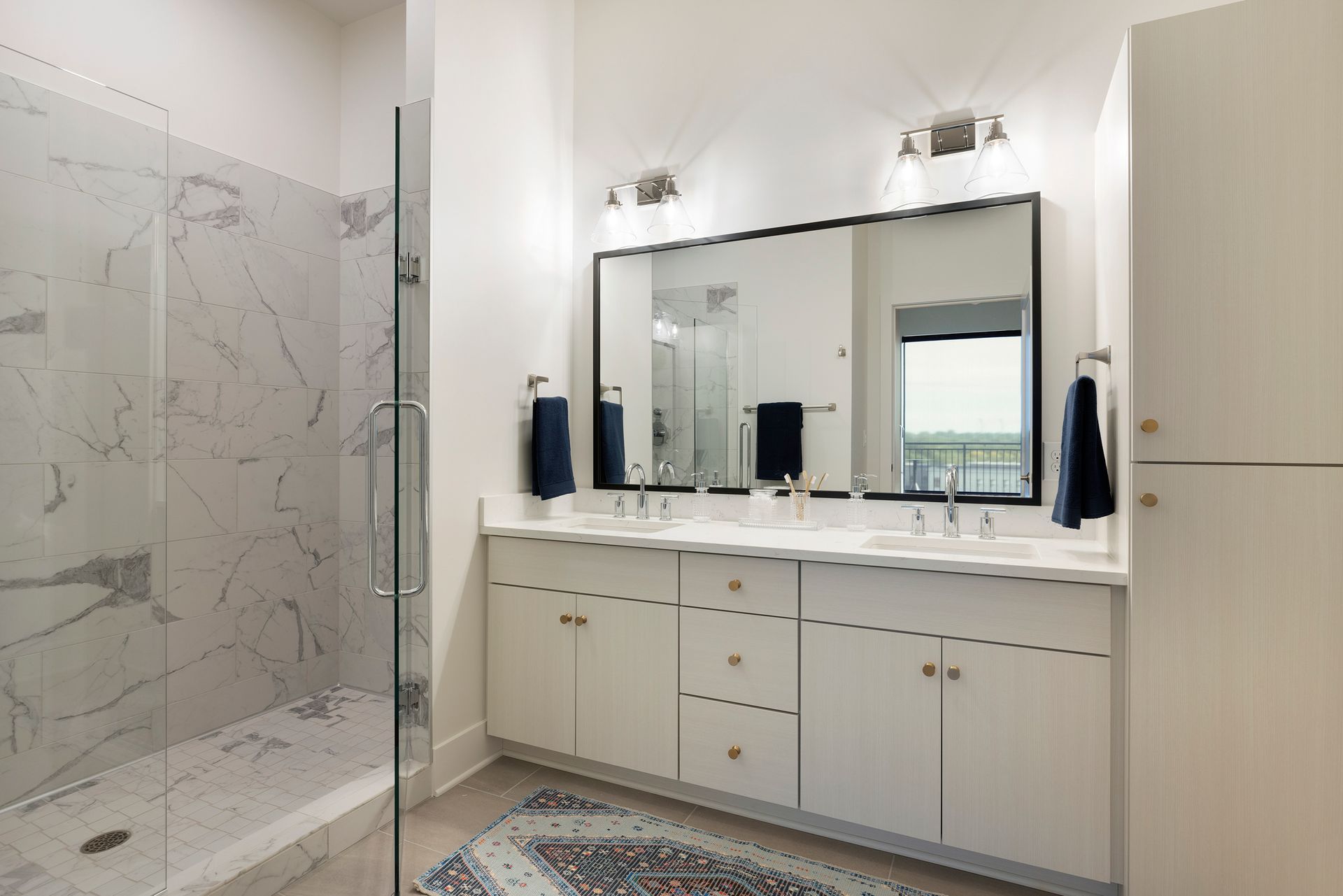 White bathroom with marble shower, double sink, and large mirror.