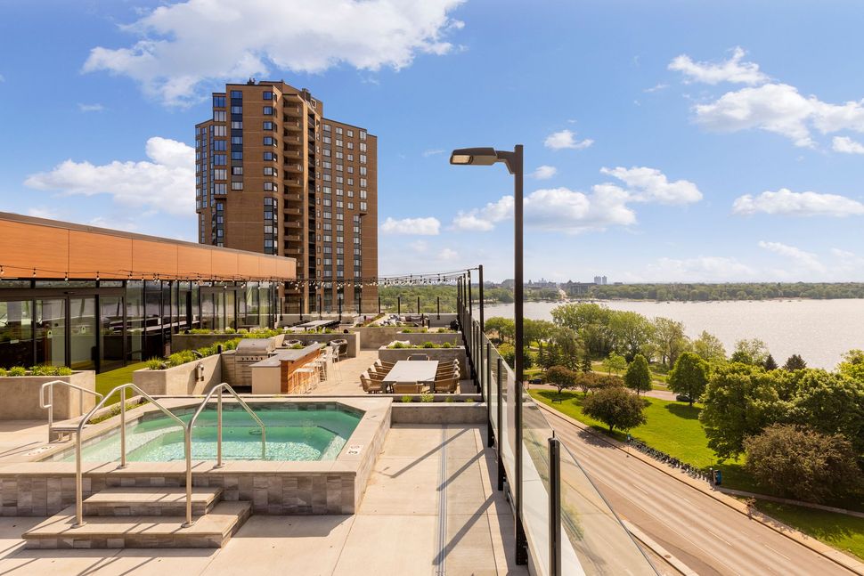 Rooftop patio with hot tub, overlooking a river and city. Sunny day, modern building.