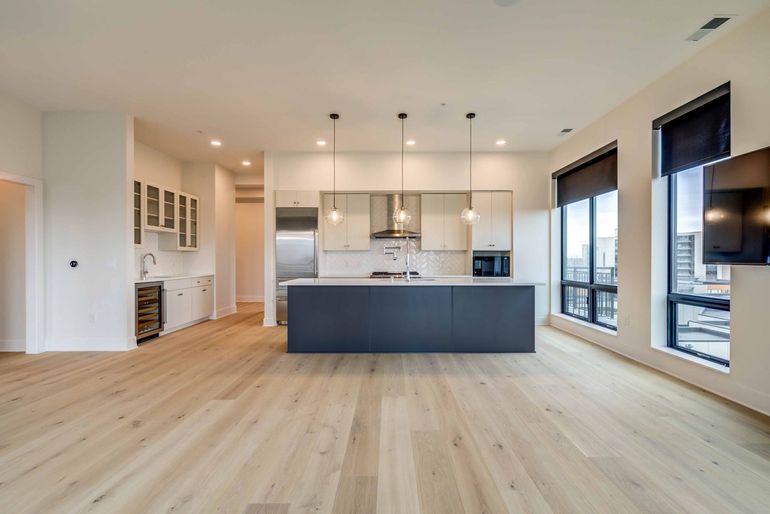 Modern kitchen with island, light wood floors, and city view windows.