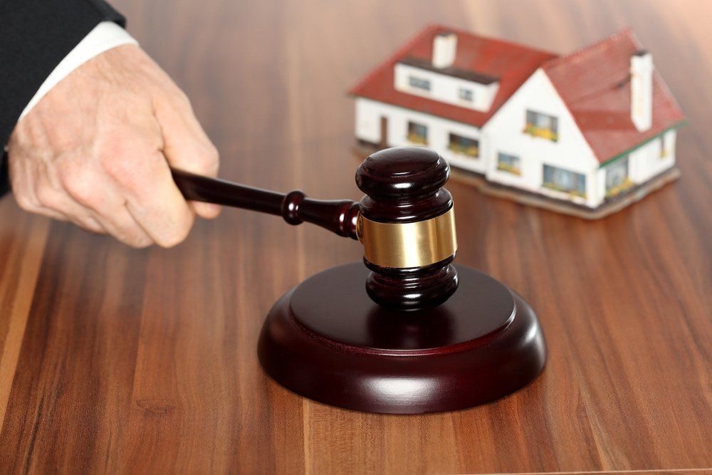 Judge's gavel hitting block with miniature house in background, symbolising property law.