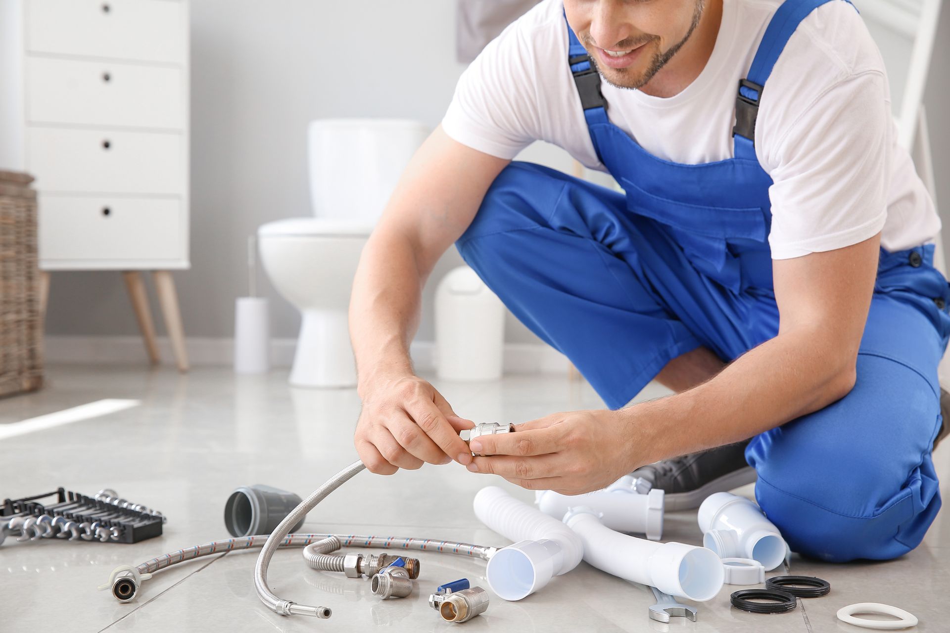Plumber in blue overalls working on plumbing in a bathroom.