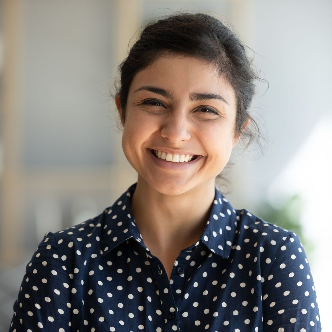 Woman with dark hair, wearing a navy polka dot shirt, smiling widely at the camera.