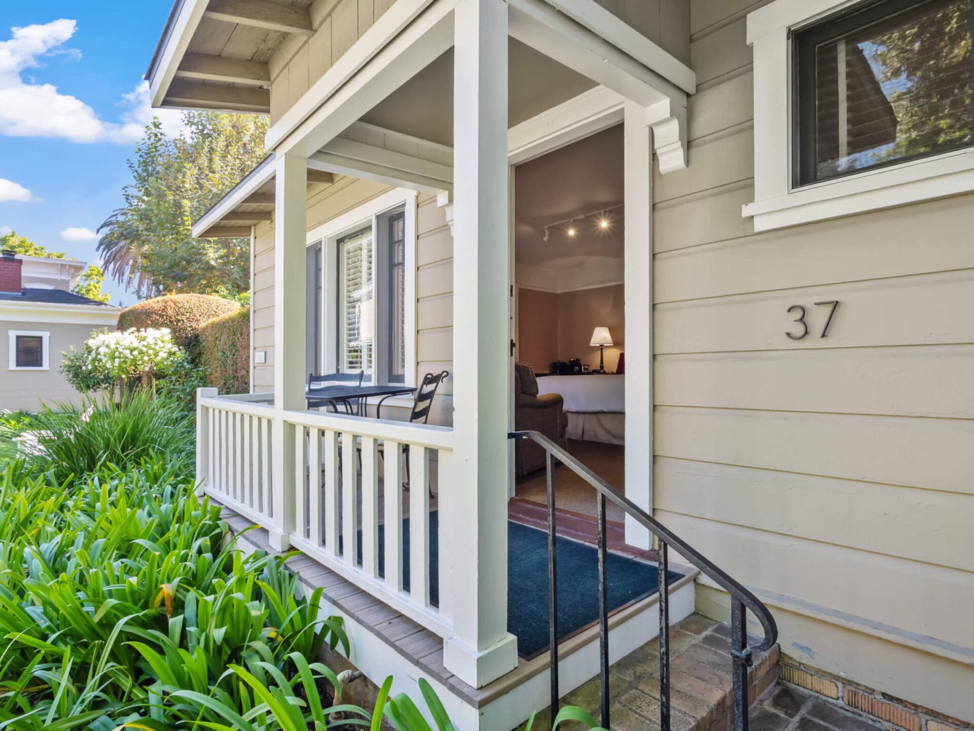 A white porch with a blue mat leads into a tan house with the number 37 on the exterior wall.