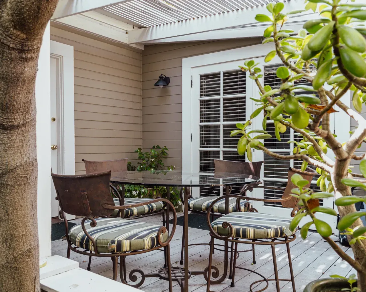 A small patio with a round glass-topped table and four metal chairs, framed by a tree and a potted succulent.