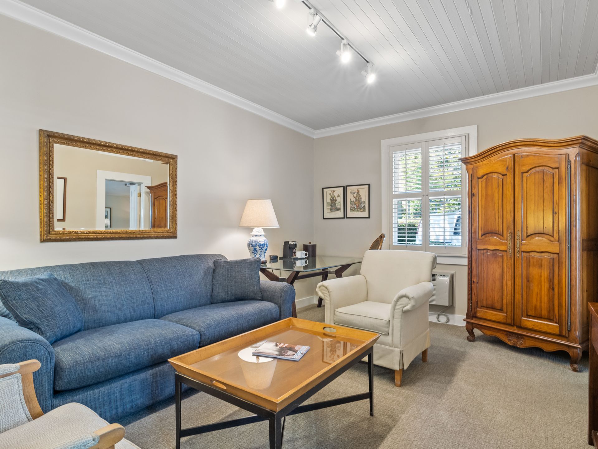 A blue sofa, white armchair, wooden coffee table, and large wardrobe in a living room with light-colored walls.