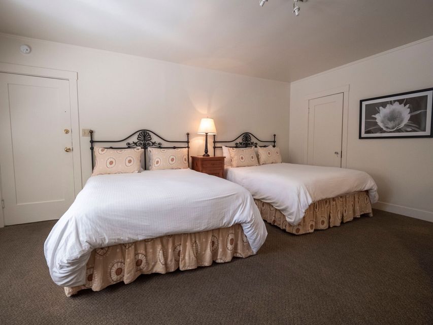 A bedroom with two queen beds, each featuring a black metal headboard and tan patterned dust ruffle, with a center lamp.