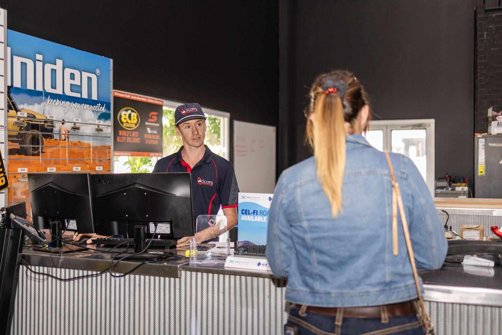 A man in a blue cap serving a woman at a counter — Scott's 4WD Parts Plus In Dubbo, NSW