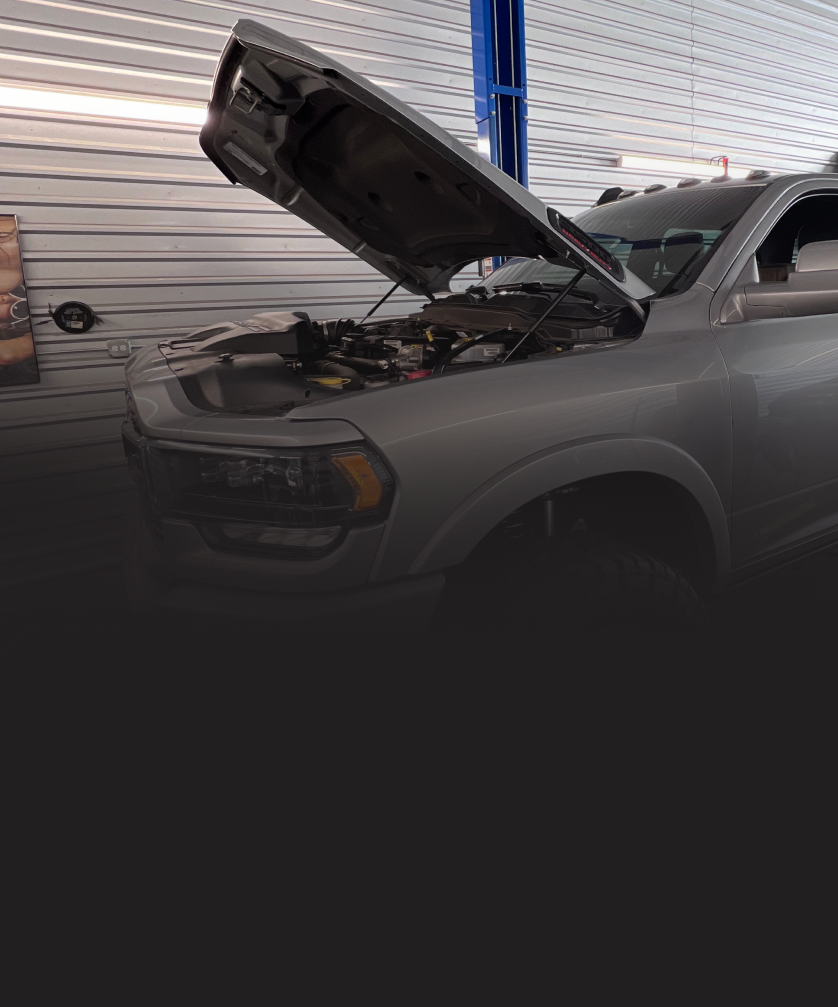 A car repair shop with two vehicles, one on a lift, and tools visible on a workbench. | Mike's Garage CC