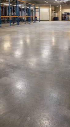 A polished gray concrete floor in a warehouse with blue storage racks along the left side under indoor lighting.