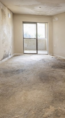 Empty, unfinished room with stained concrete floors, damaged walls, and a sliding glass door leading to a balcony.