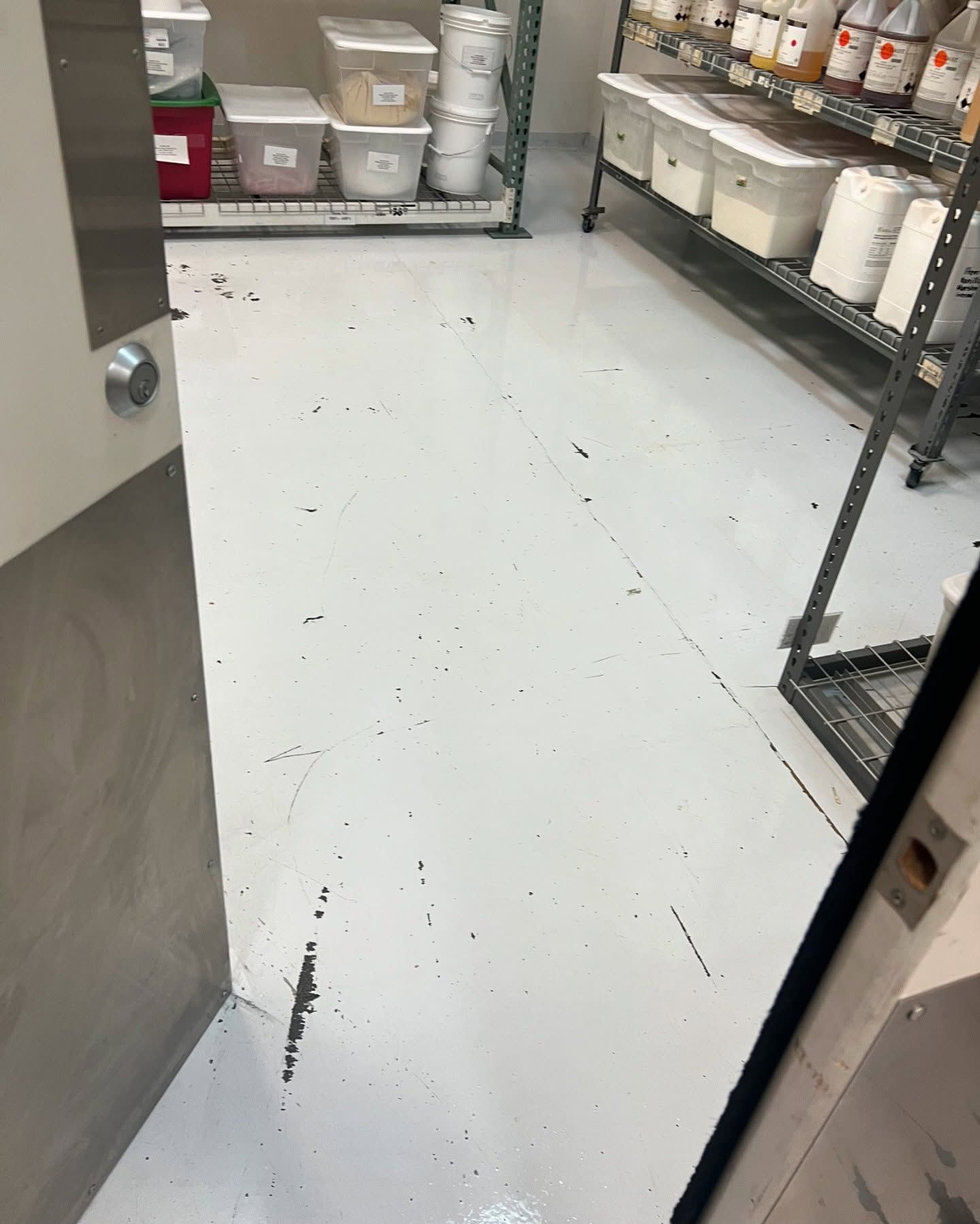 White commercial kitchen floor with black scuffs, metal shelving, and various containers.