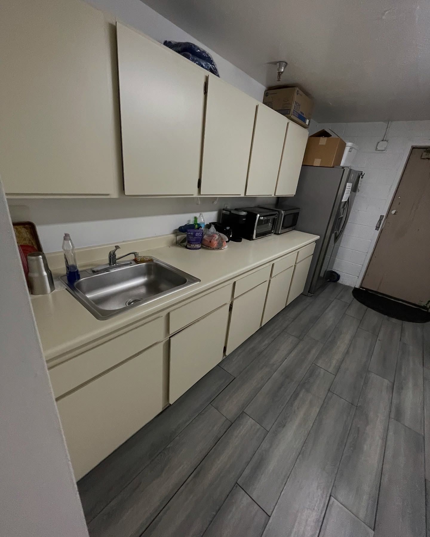 Kitchen with off-white cabinets, stainless sink, and appliances. Gray flooring and brown door.