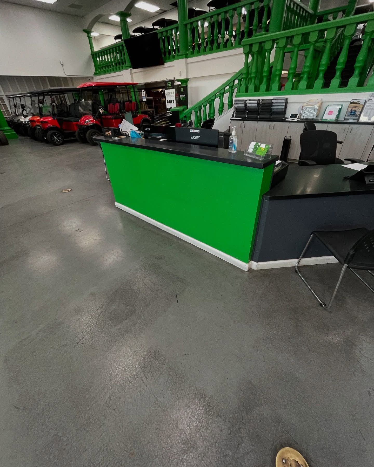 Green front desk in a store with red golf carts. Green and white accents with gray floor.