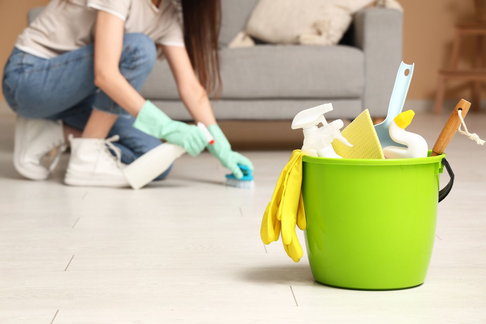 Woman cleaning floor, green bucket of cleaning supplies in foreground.