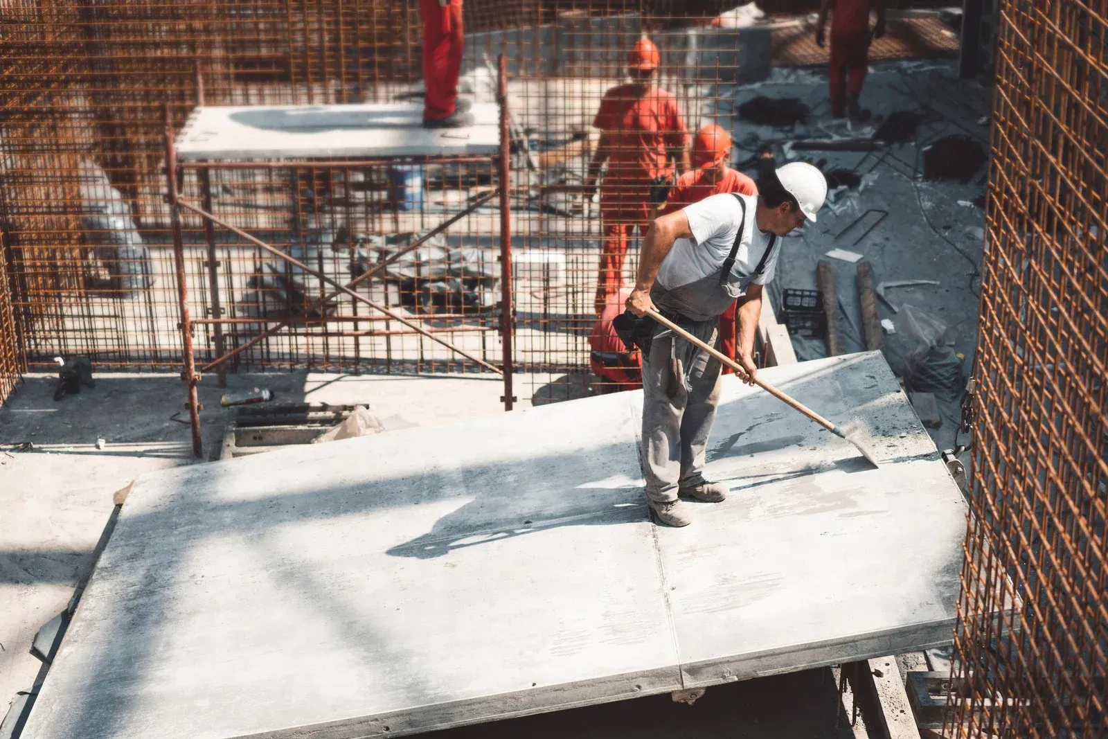 Construction workers at a building site, one worker using a tool to smooth a concrete slab.