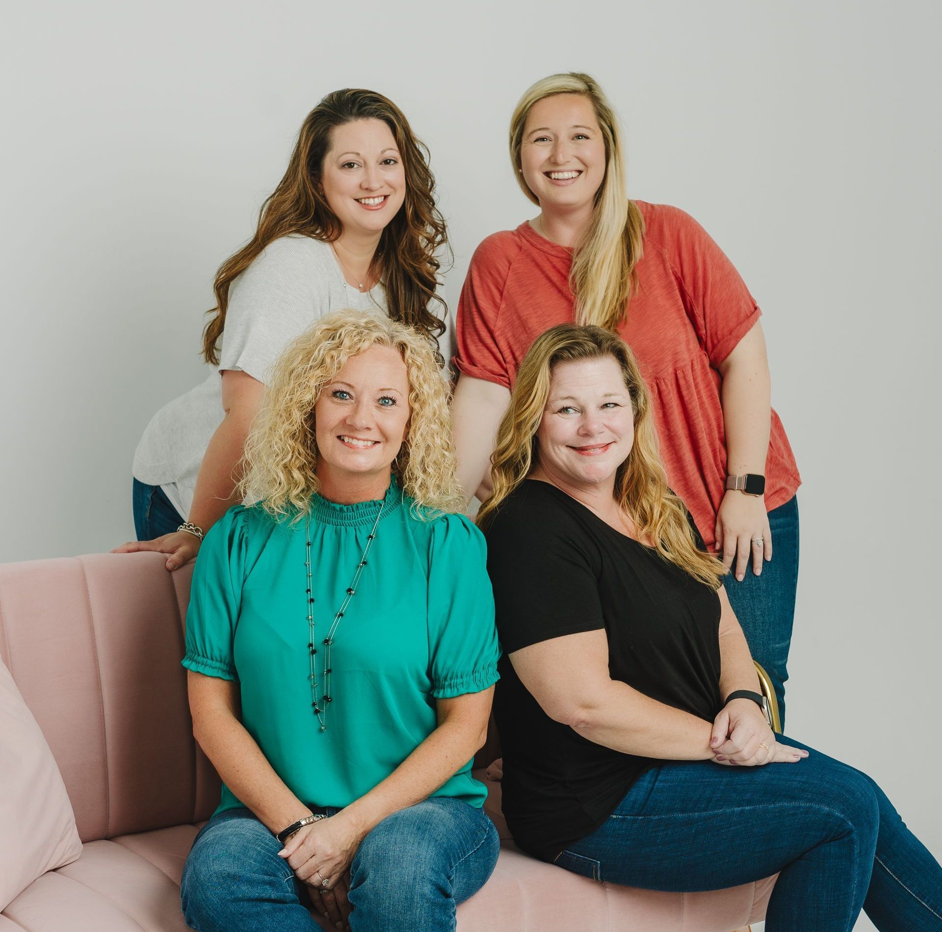 Four women are posing for a picture while sitting on a pink couch.