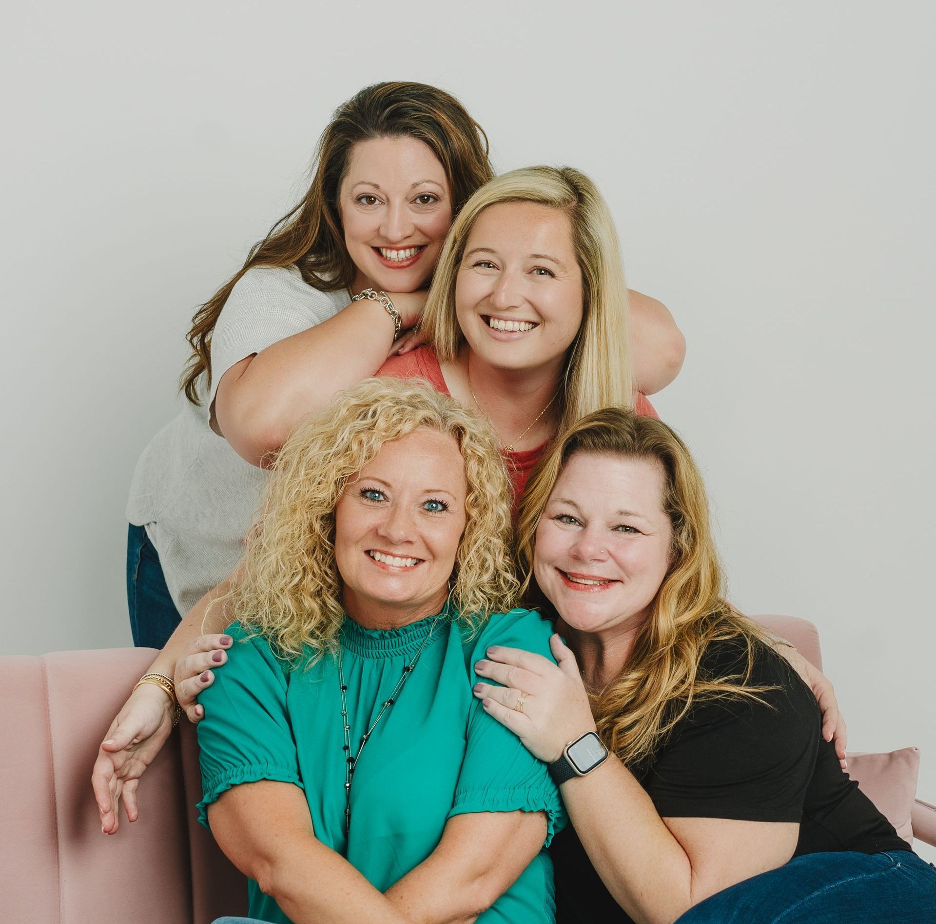 Four women are posing for a picture while sitting on a pink couch