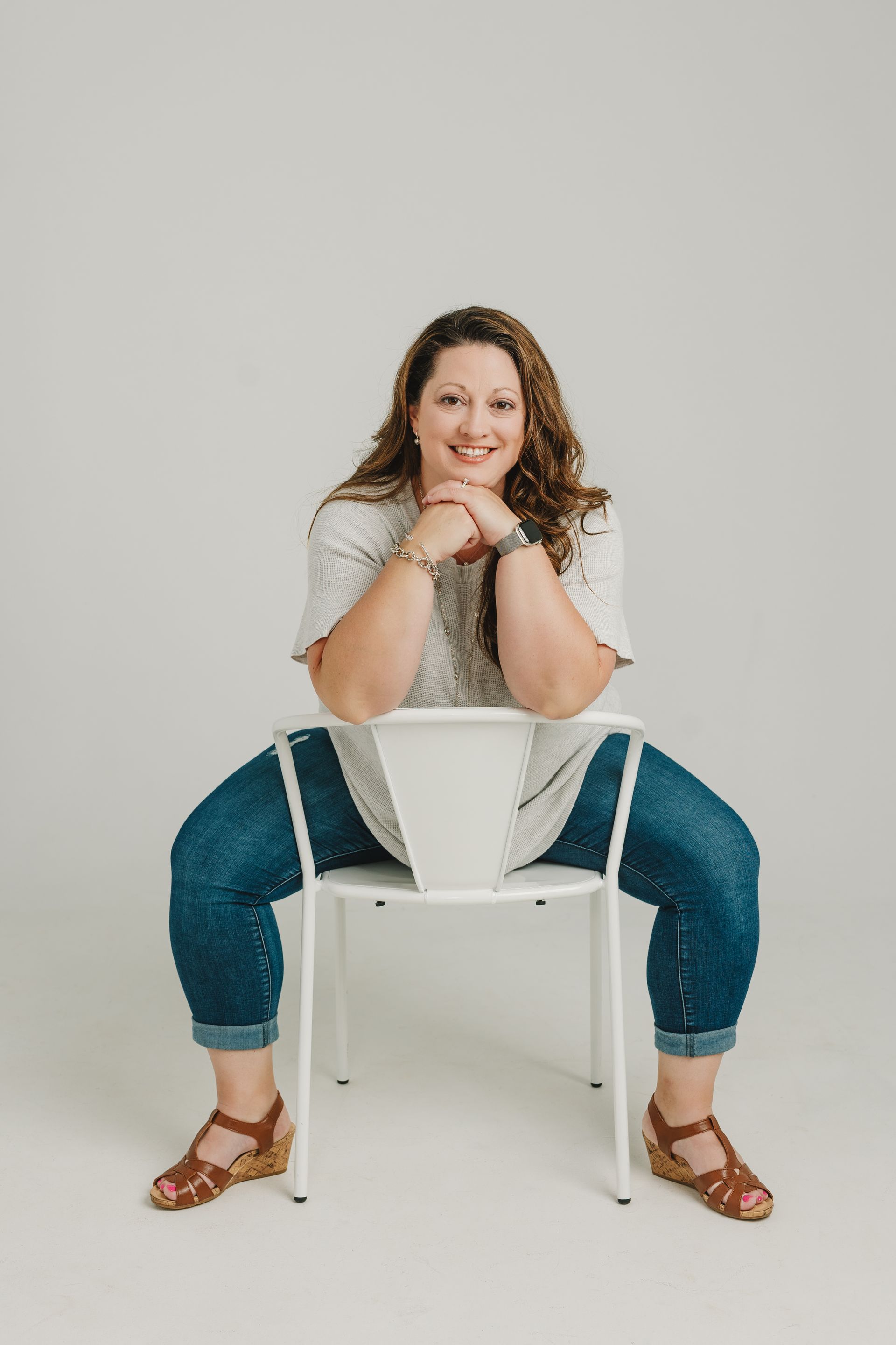 A woman is sitting on a white chair with her legs crossed.