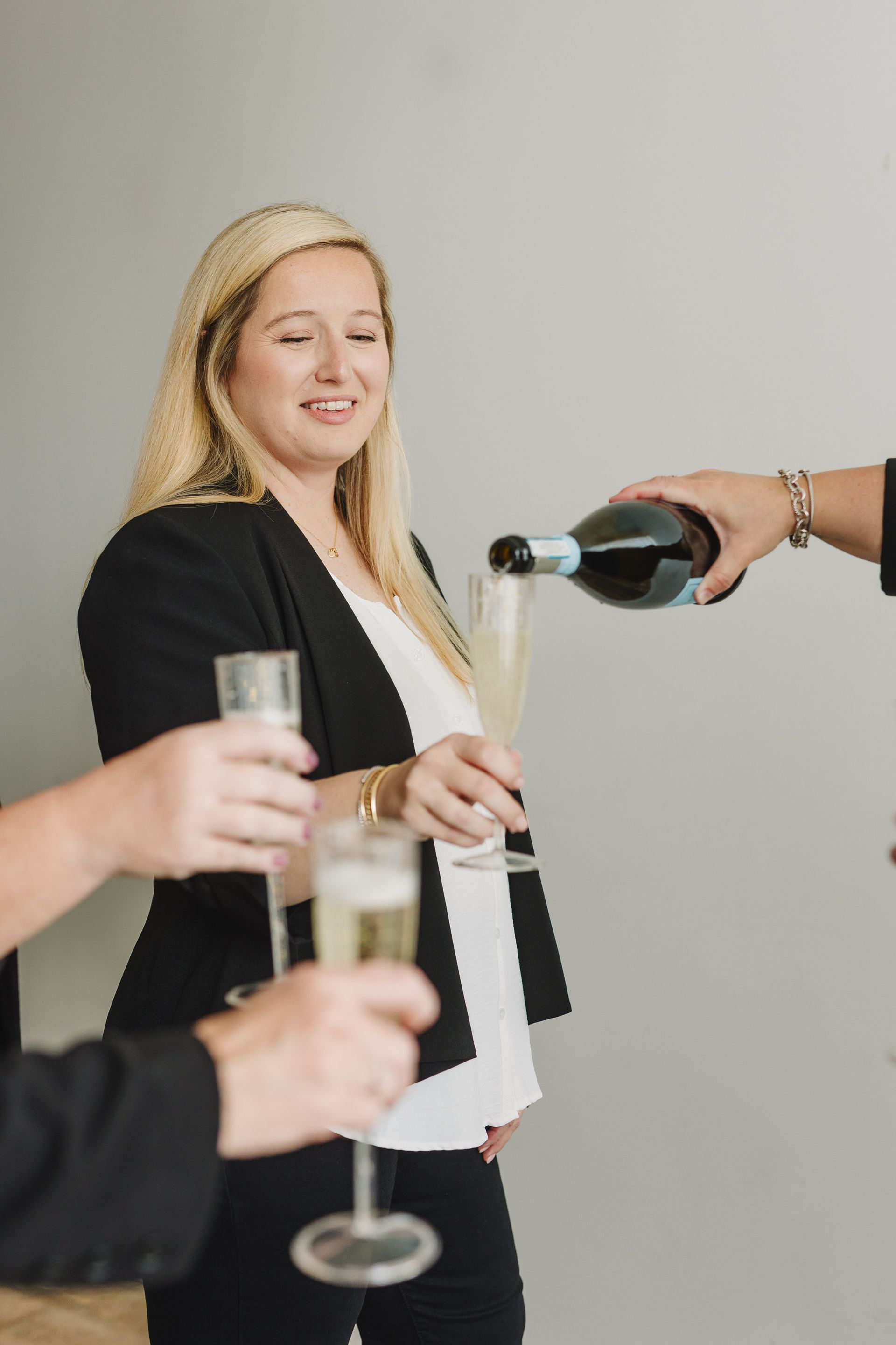 Woman in black blazer smiles as champagne is poured into her glass at a gathering.