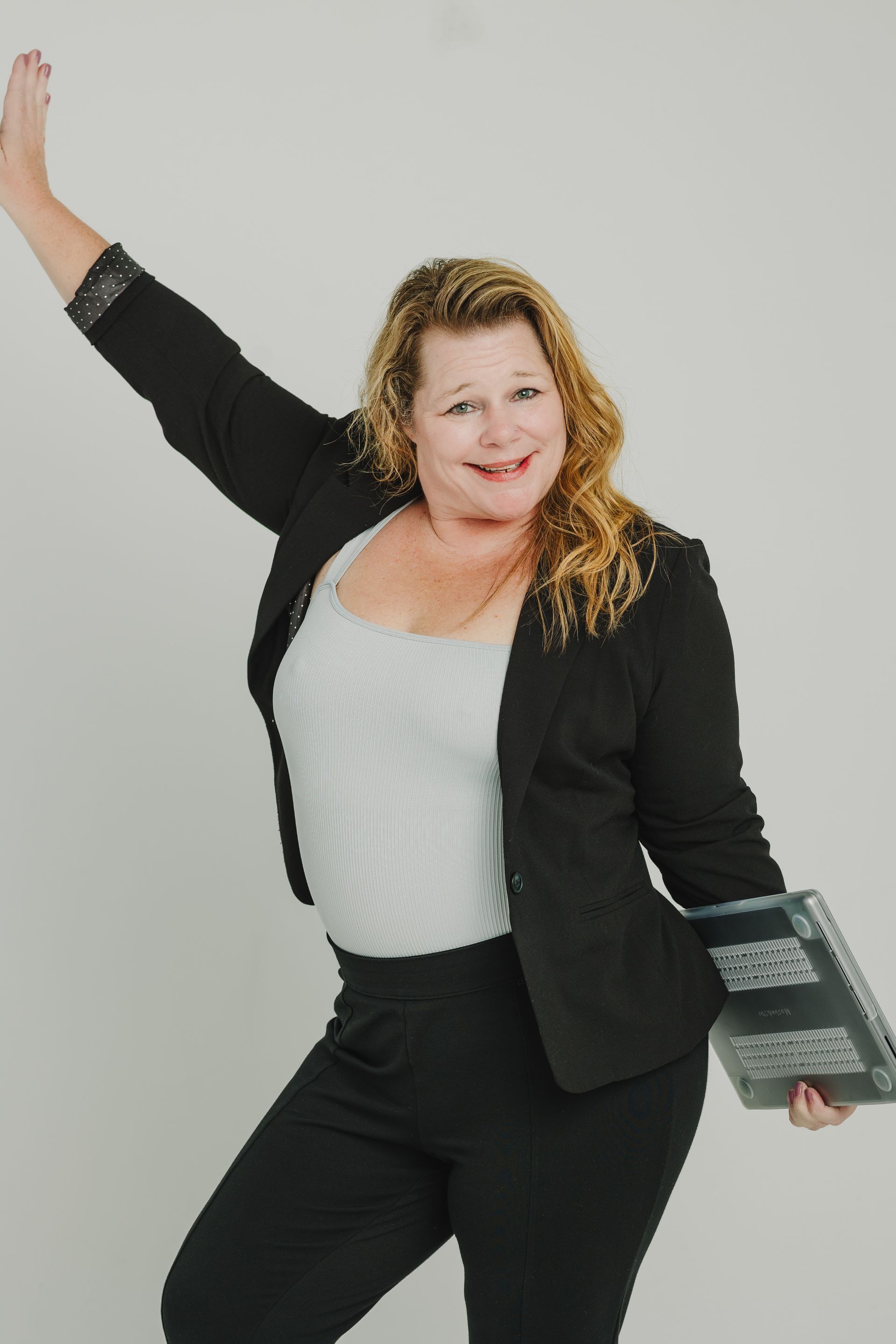 A woman in a black jacket and black pants is standing with her arms in the air.