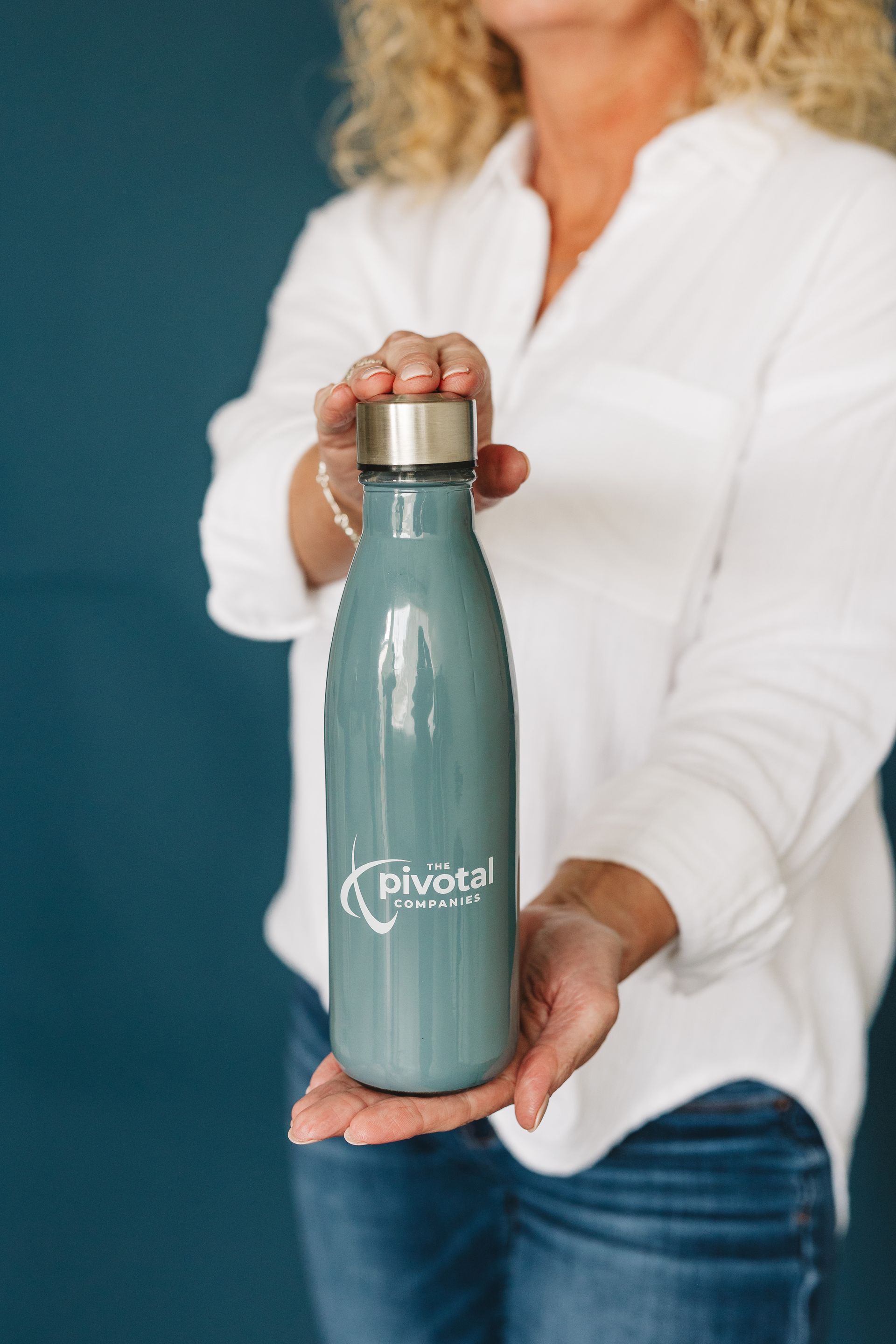 Person holding a teal water bottle with a silver lid against a blue backdrop.
