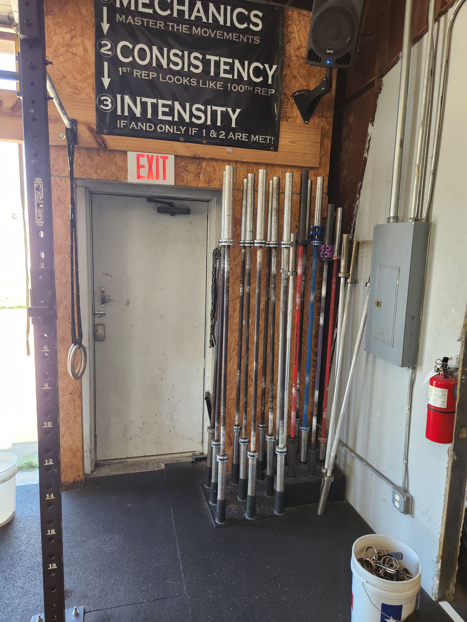 Weightlifting bars in a rack next to an exit door inside a gym in Lavon, TX.