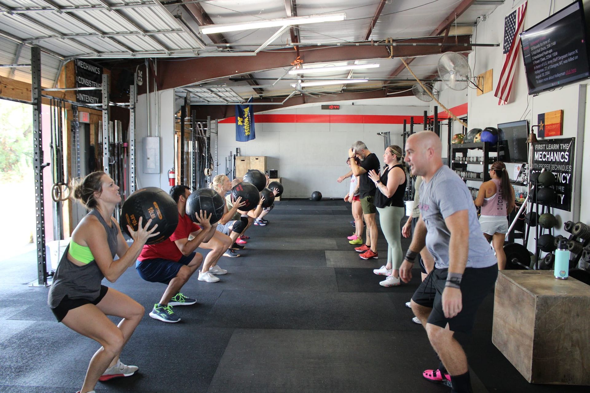 People at CrossFit Lavon gym in Lavon, TX, squatting and holding medicine balls, with a coach observing.