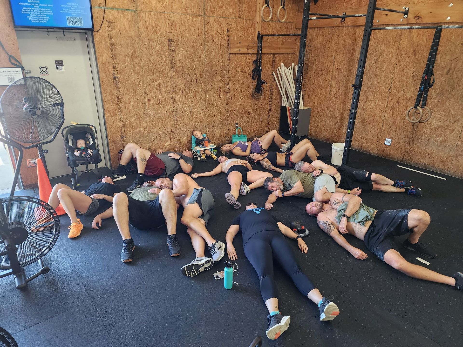 People resting on the CrossFit Lavon gym floor after a workout, many lying down, some with water bottles nearby.