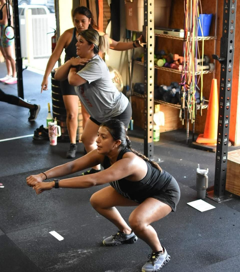 People doing squats in a gym in Lavon, TX; instructor watches.