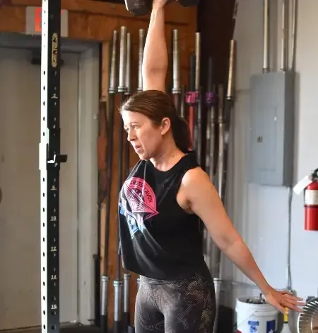 Woman lifting a dumbbell overhead in a gym in Lavon, TX, with focus and determination.