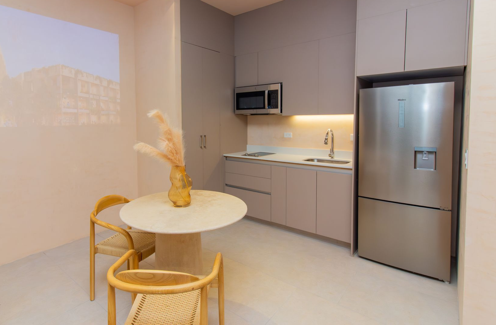 Small modern kitchen with gray cabinets, stainless steel refrigerator, and round table with chairs.