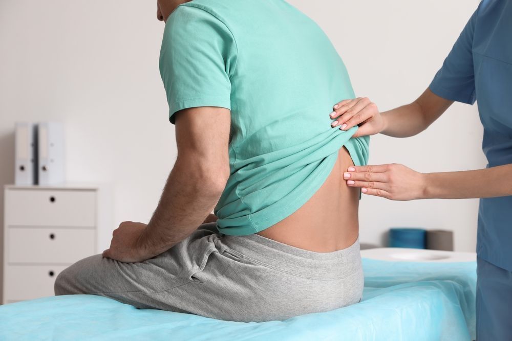 Patient seated on exam table, doctor examining lower back.