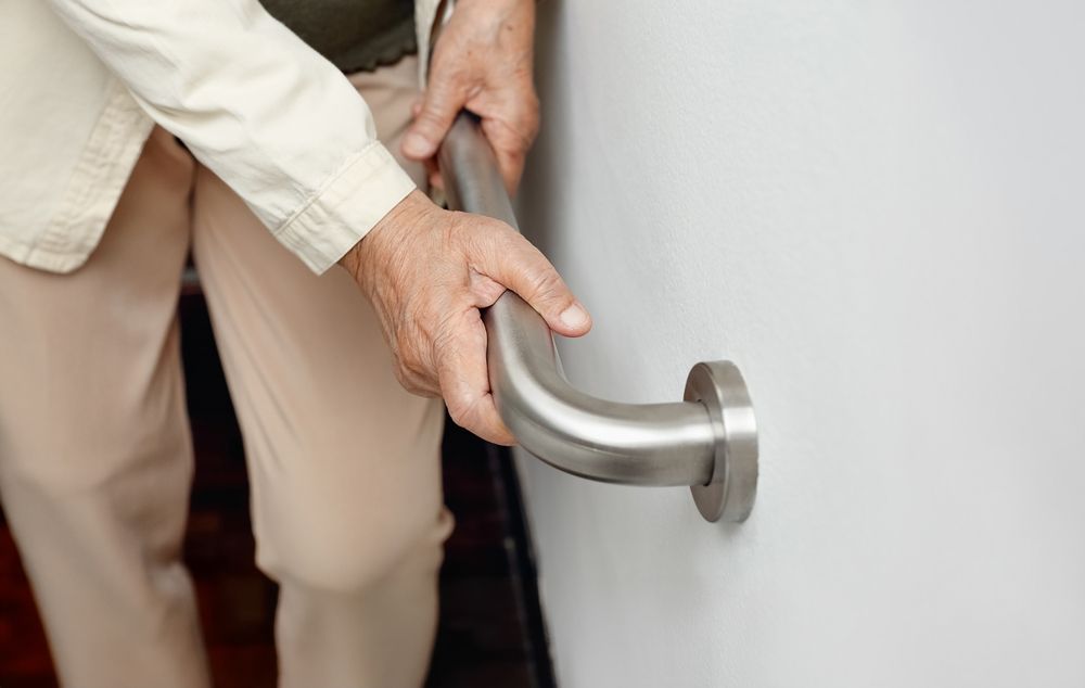 Person holding a metal handrail mounted on a white wall for support.