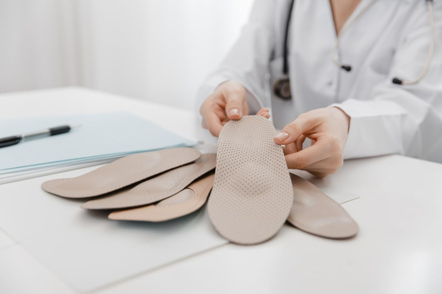 Doctor holding orthotic insoles, office setting.