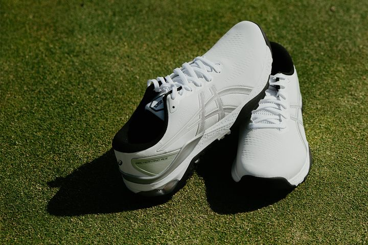 White soccer cleats on grass, one showing a black heel and side stripes.