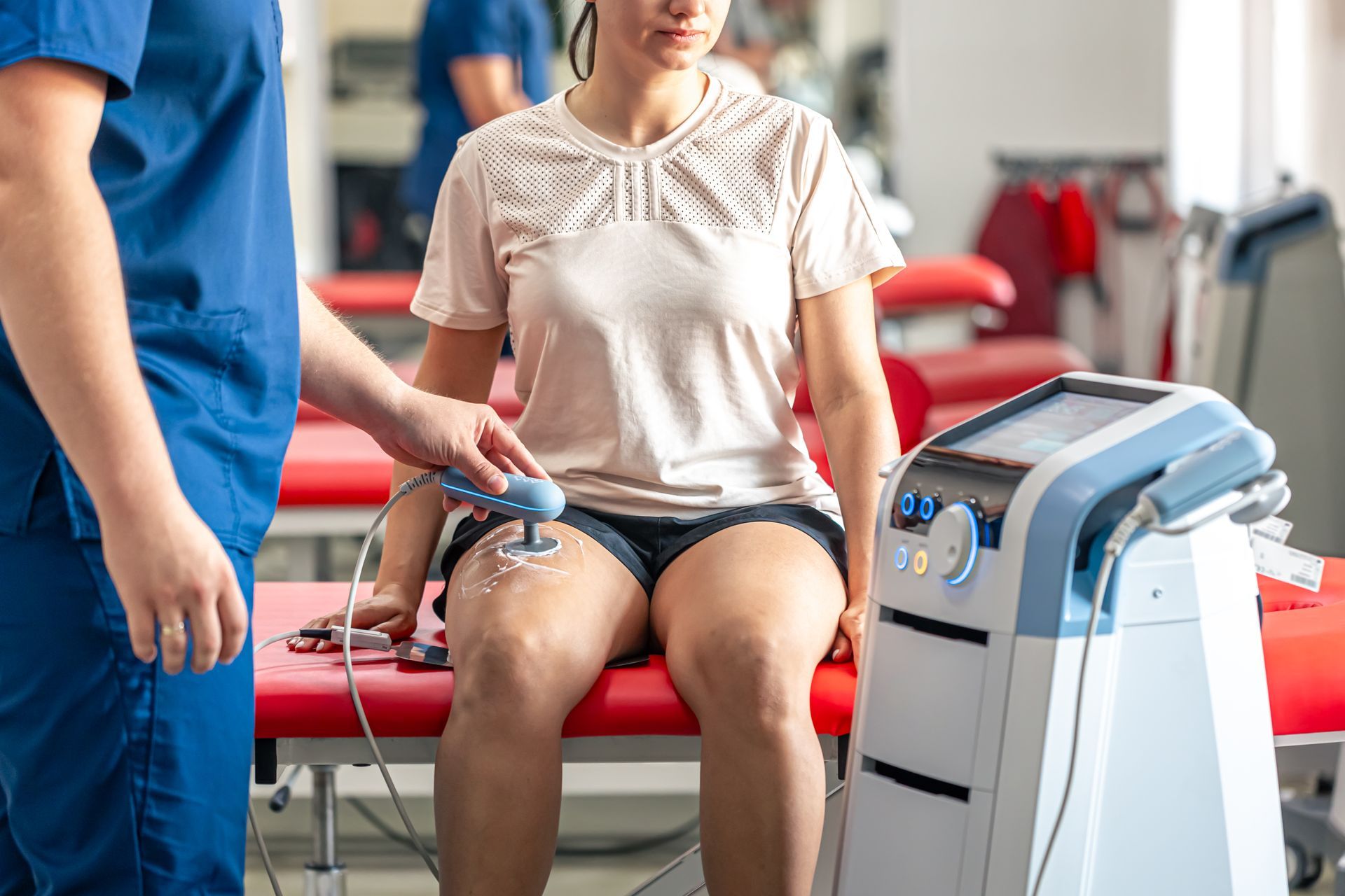 A woman is sitting on a bed getting an electrical therapy treatment.