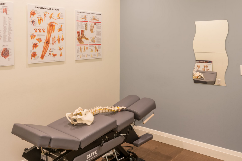 Chiropractic exam room with adjustment table, spine posters, and wall mirror
