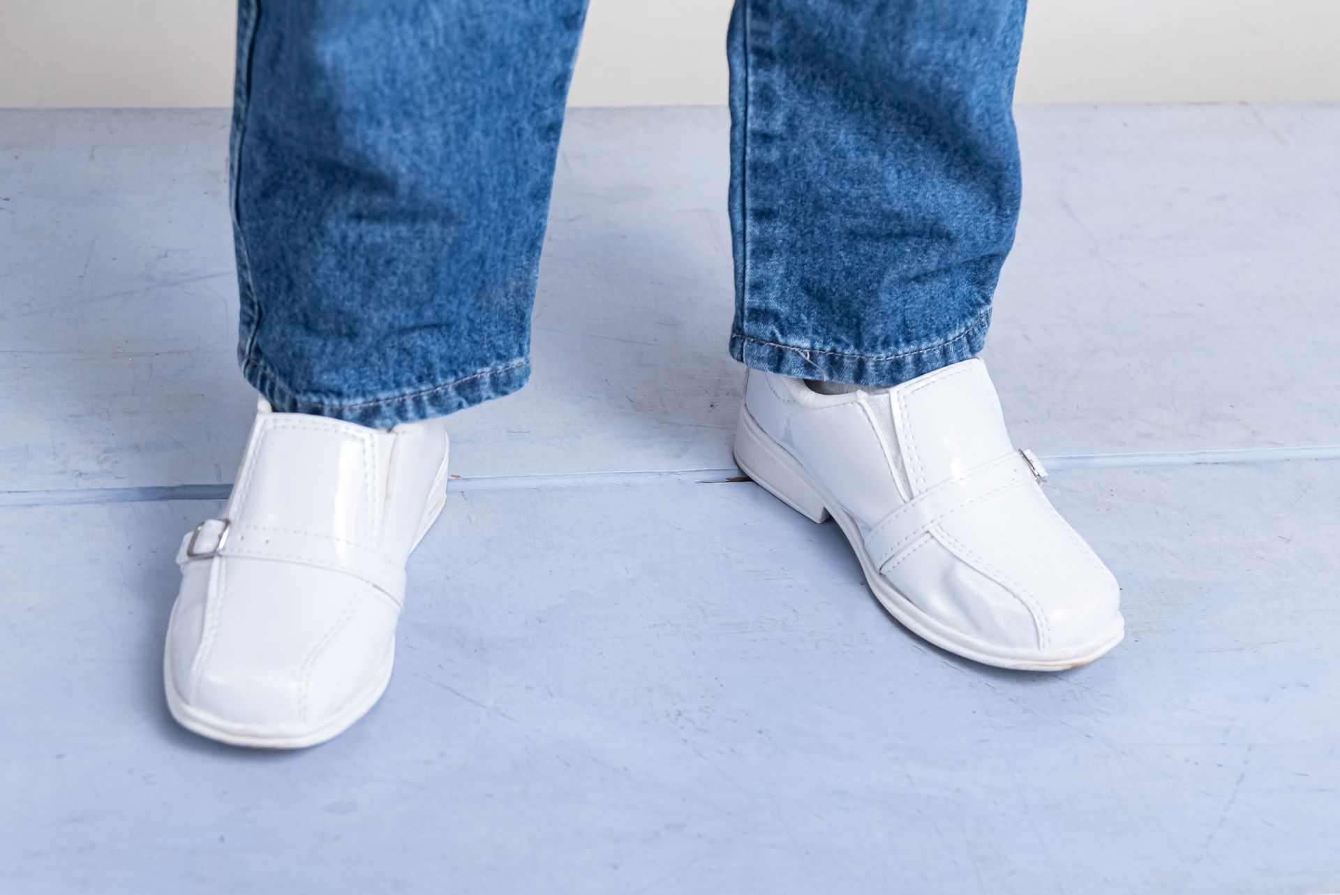 A person wearing blue jeans and white shoes is standing on a blue surface.