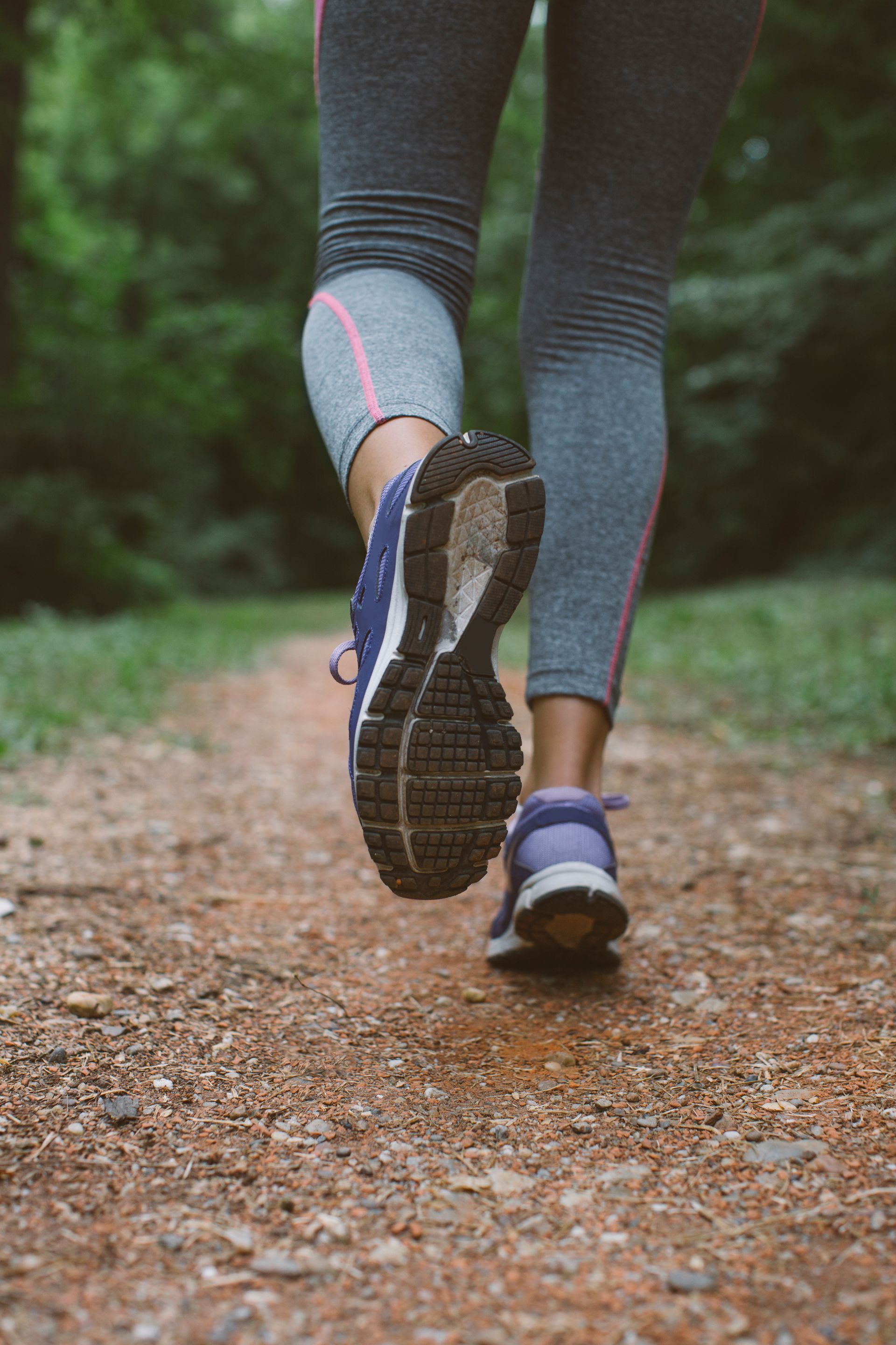 A woman is running on a dirt path in the woods.