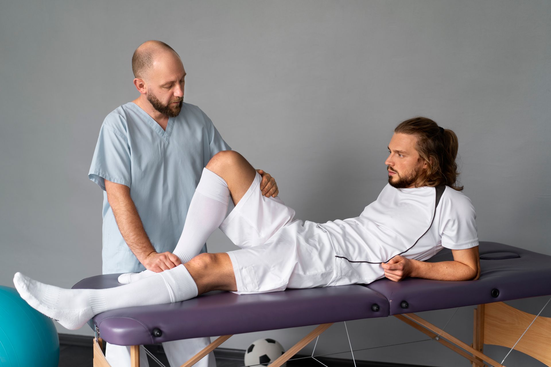 A soccer player is getting his leg examined by a doctor.